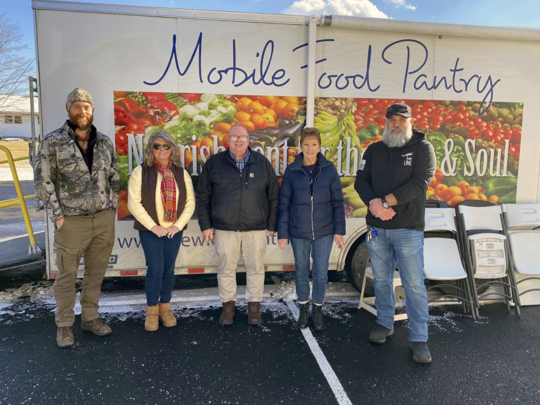 People stand together in front of the New Love Center mobile food pantry truck outside a church at a new food distribution site launch