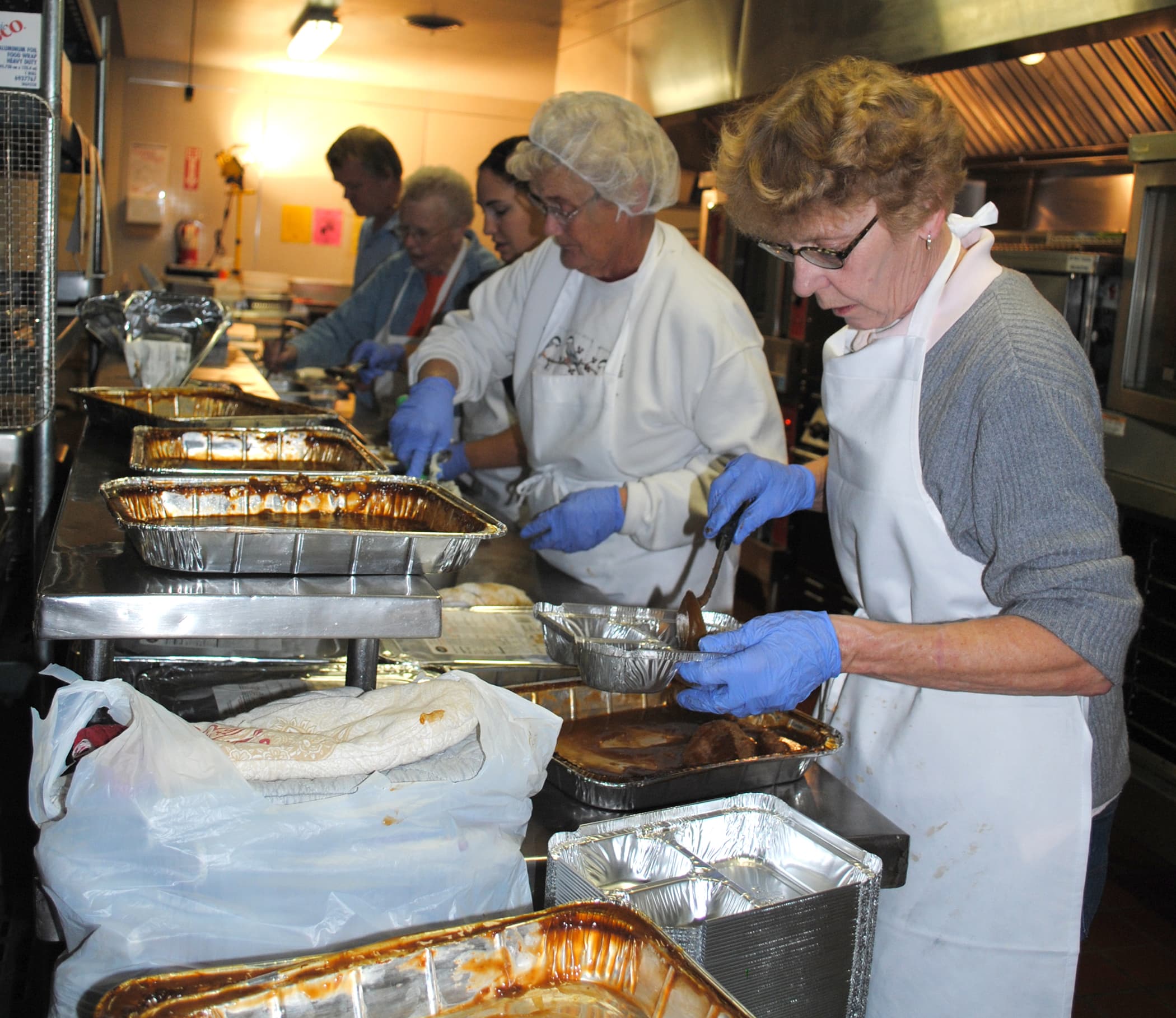 Volunteers in a community kitchen stir large pots of food while preparing Meals on Wheels deliveries
